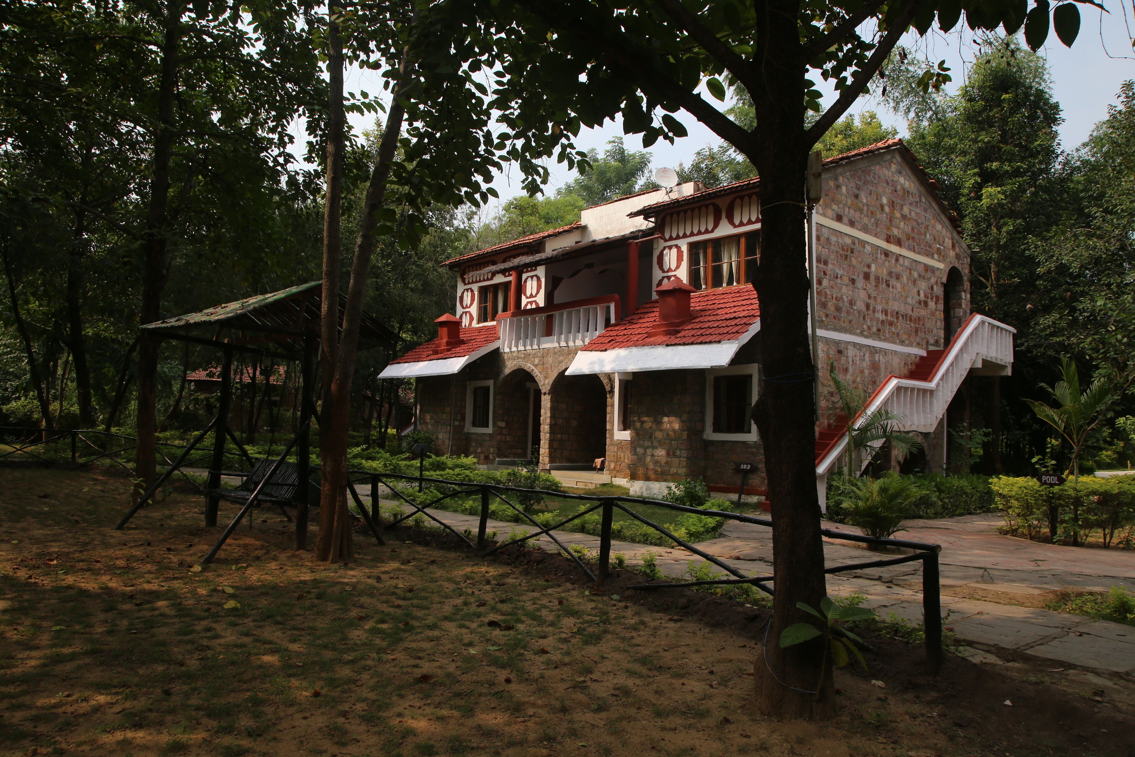 A rustic stone building with a red-tiled roof, surrounded by trees and a fenced area.