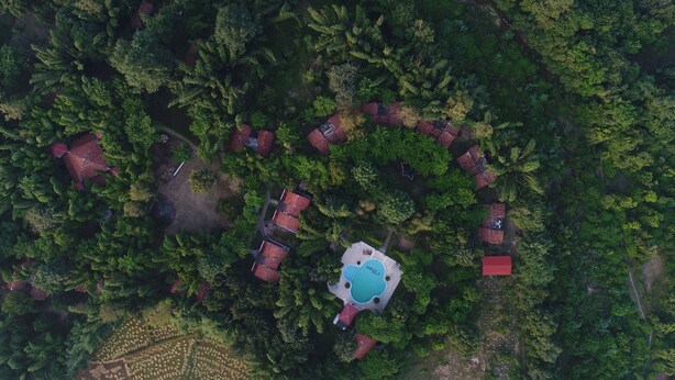 An aerial view of a resort with multiple red-roofed cabins arranged in a semi-circular pattern around a central swimming pool.