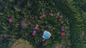 Une vue aérienne d’un complexe hôtelier avec plusieurs chalets aux toits rouges disposés en forme de demi-cercle autour d’une piscine centrale.