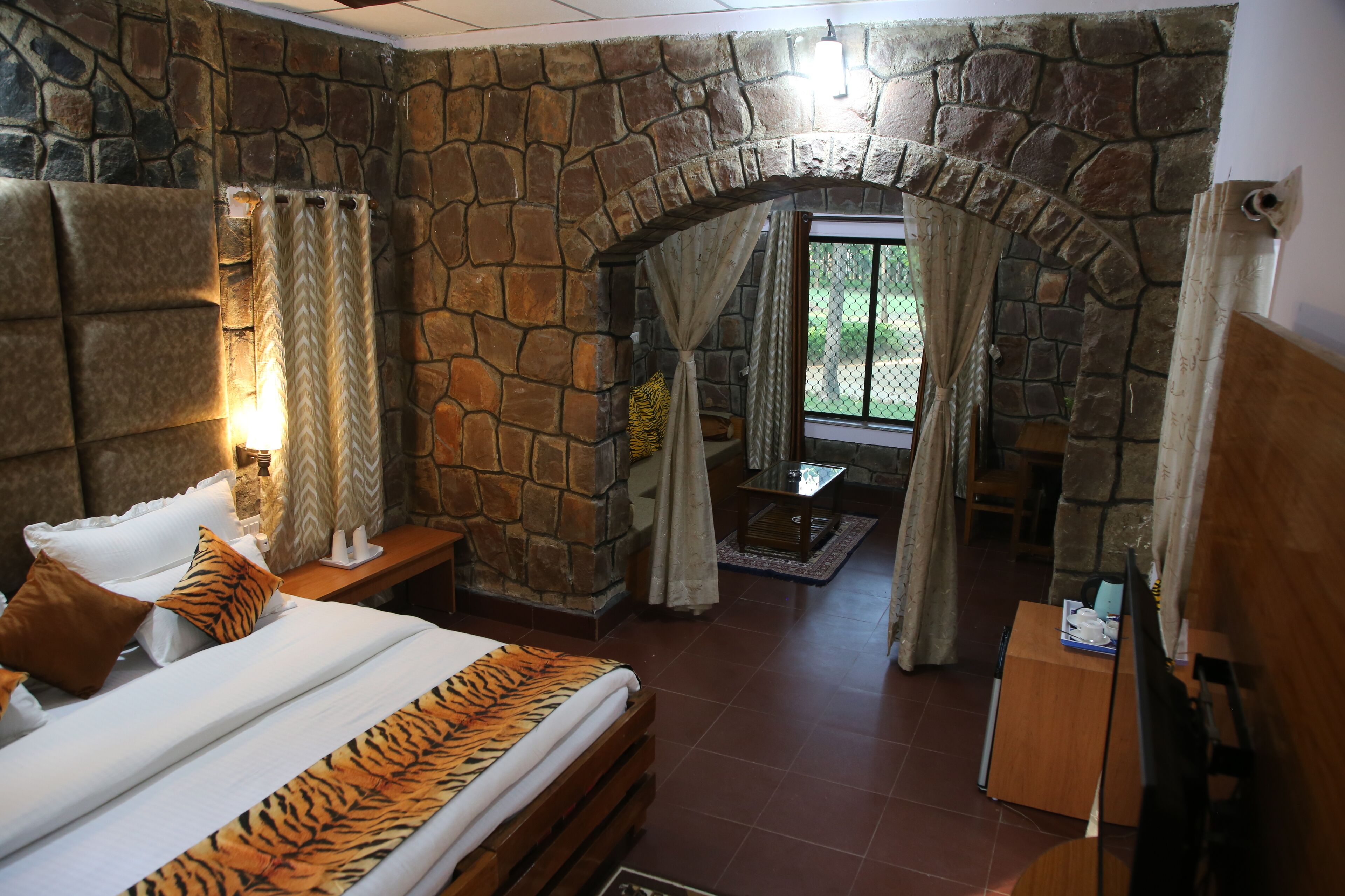 A bedroom with a stone wall, a bed with a tiger print bedspread, a nightstand, and a wooden headboard.