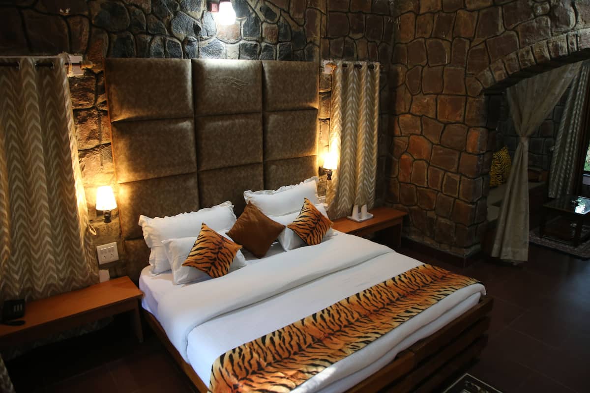 A bed with a tiger print bedspread, a stone wall, and a nightstand with a lamp.