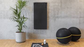 En yogamatta, två träningsbollar, en växt och en påse ris ligger på ett trägolv med en betongvägg i bakgrunden.