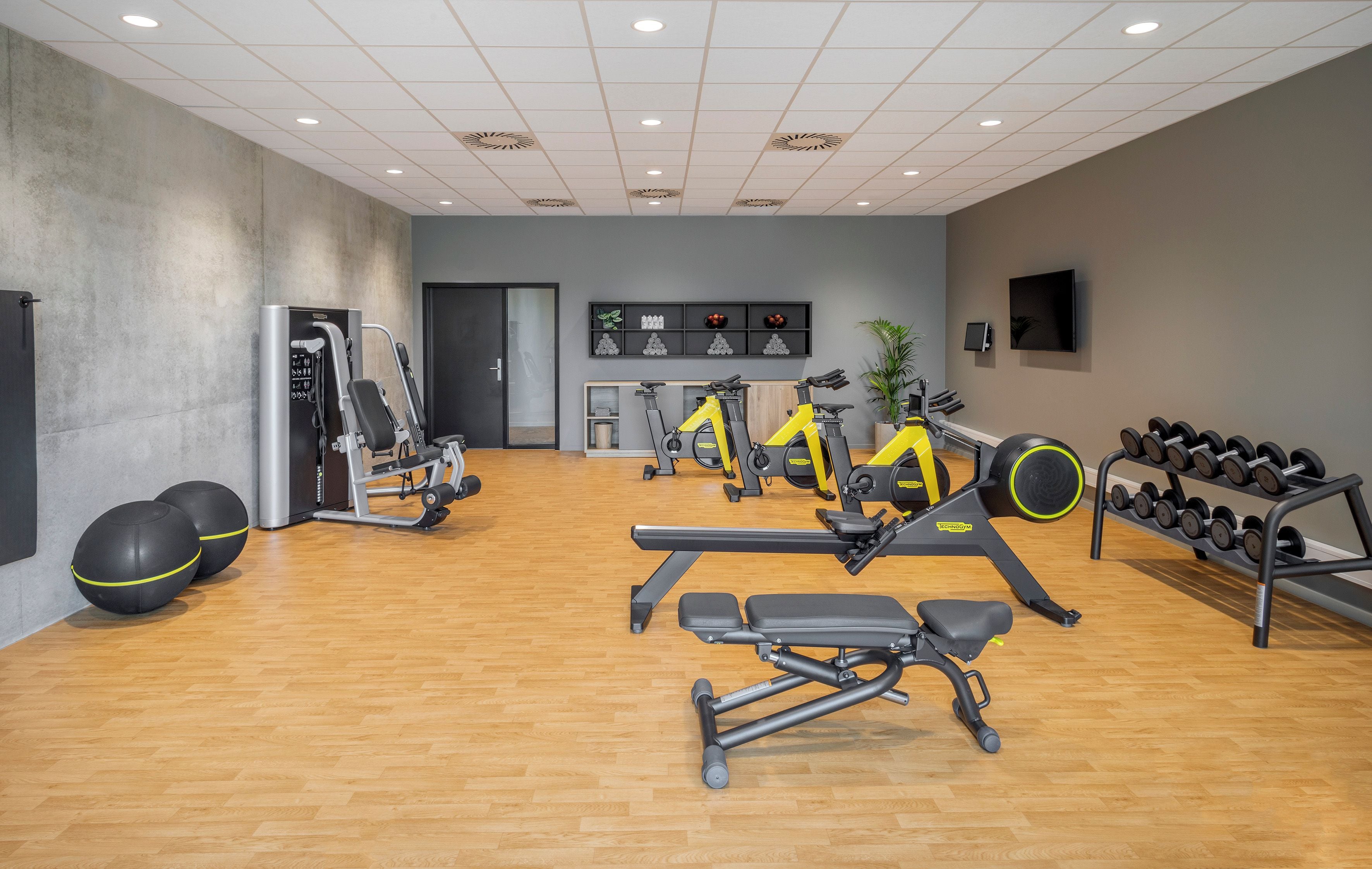 Une salle de sport équipée de matériel d’exercice, dotée d’un plancher en bois et d’un mur gris.