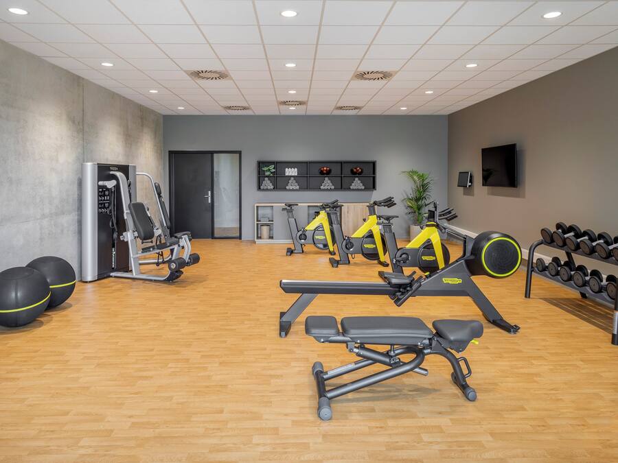 Une salle de sport équipée de matériel d’exercice, dotée d’un plancher en bois et d’un mur gris.