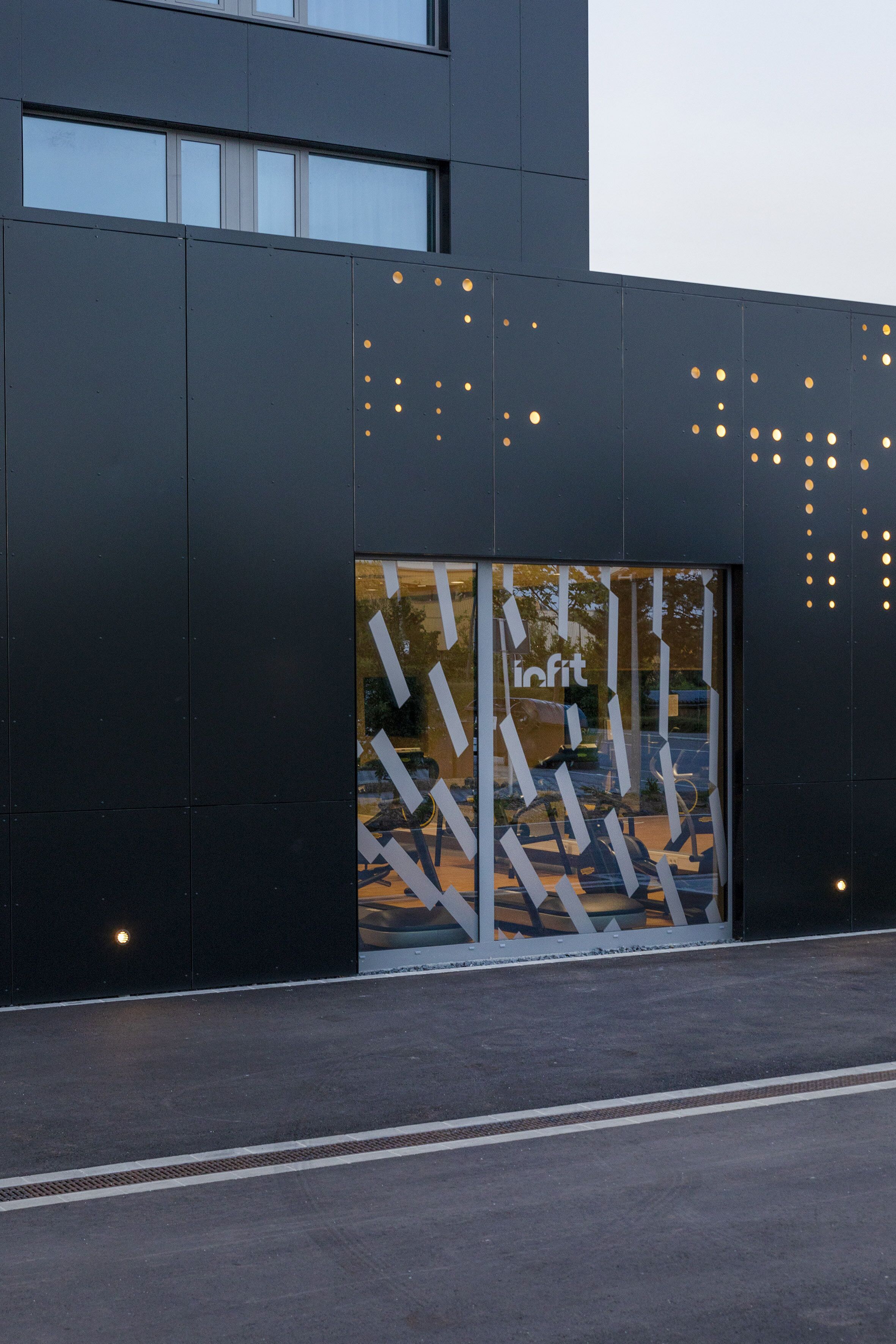 Fachada moderna de un edificio con un amplio ventanal de vidrio que presenta patrones geométricos y la palabra "lifit" reflejada.