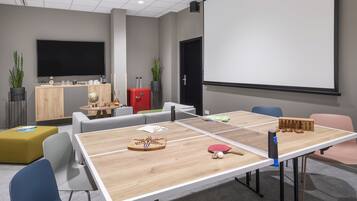 Une salle de conférence équipée d’une table de ping-pong, de chaises, d’un écran de projection et d’un coin café.