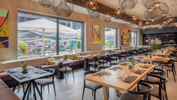 Un restaurante moderno con mesas altas, cabinas, ventanas amplias y lámparas colgantes.