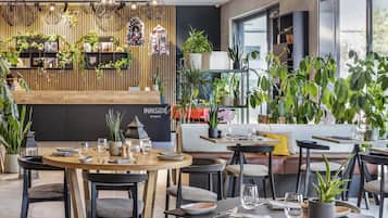 Un restaurante moderno con detalles de madera, varias áreas de estar y abundante vegetación interior.