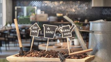 A wooden planter with soil and a shovel, accompanied by signs that read "EAT LOCAL," "de GAART," and "GROW LOCAL."