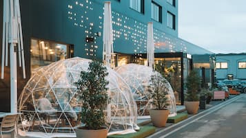 A modern building with large windows, outdoor seating areas with transparent dome structures, and potted plants.