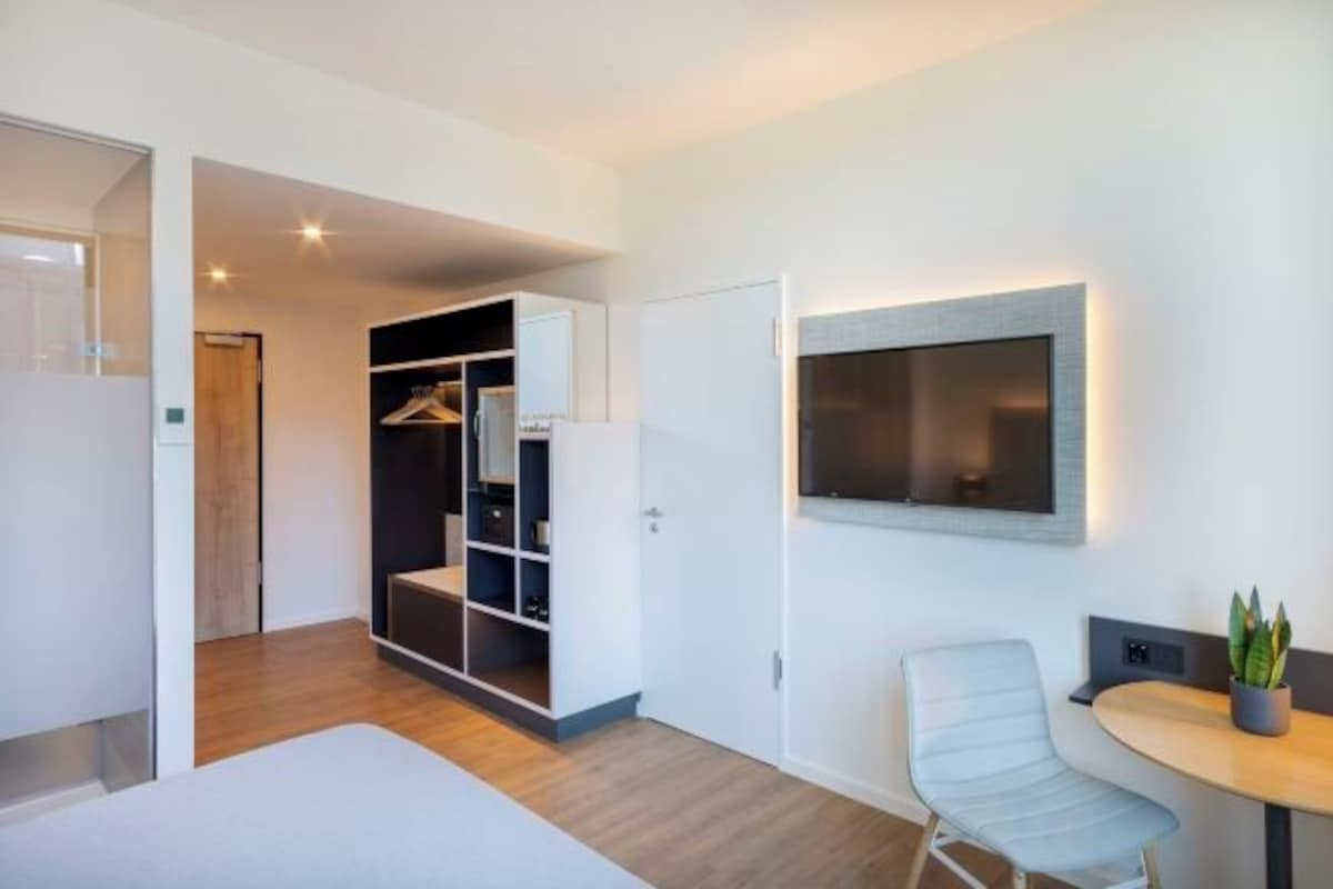 Una habitación moderna con cama, zona de estar, armario y televisor montado en la pared.