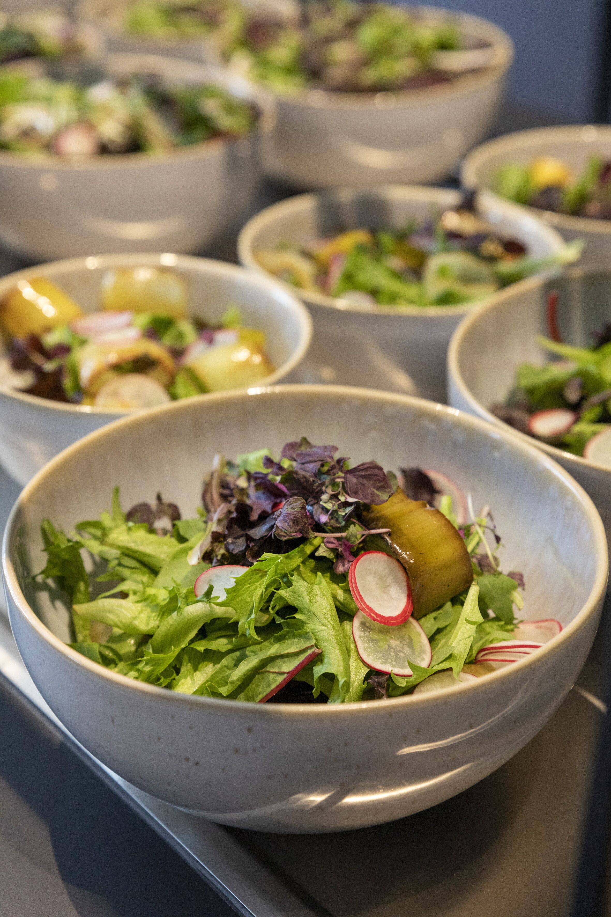 A buffet with multiple bowls of salad, including greens and radishes.