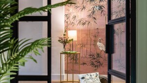 Ein Zimmer mit Holzboden, einer Wand mit Bambusmuster, einem kleinen Tisch mit Lampe und einem Blumentopf.