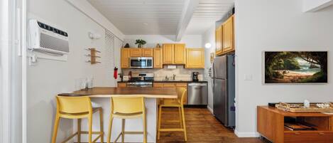 A modern kitchen with wooden cabinets, a stainless steel refrigerator, and a dining area with yellow chairs.