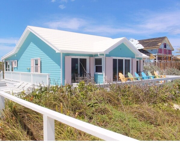A coastal house with a white roof and turquoise siding, featuring a covered porch with blue chairs. - South Beach: A Perfect Beachfront Getaway - Pool, beachfront, ocean views, (Hope Town Bahamas)