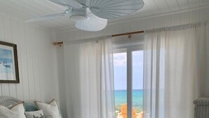 A bedroom with a bed, a ceiling fan, a window with curtains, and a view of the ocean. - South Beach: A Perfect Beachfront Getaway - Pool, beachfront, ocean views, (Hope Town Bahamas)