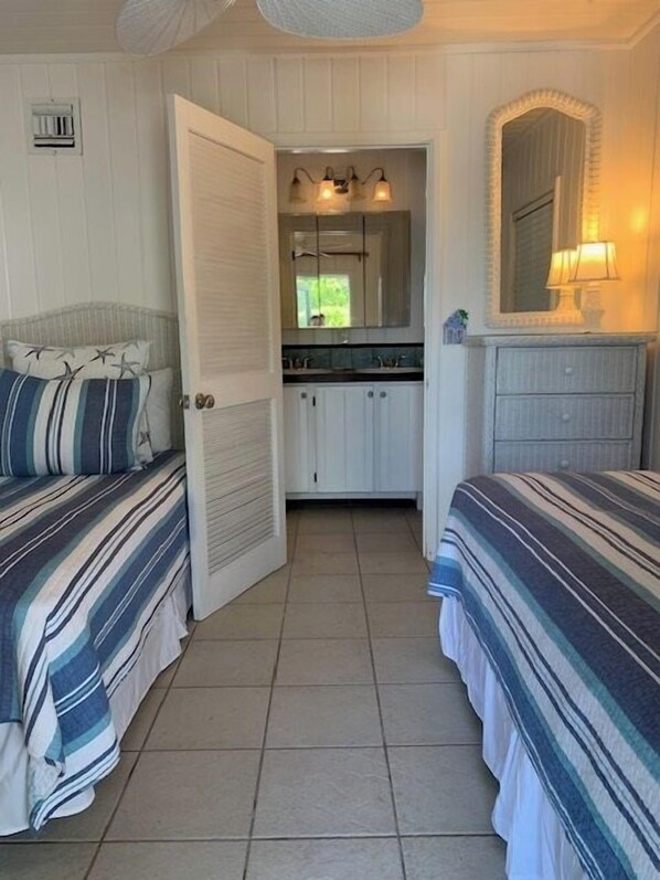 Un dormitorio con dos camas, un baño con espejo y lavamanos, y una puerta que da a otra habitación.