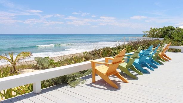 A deck with colorful Adirondack chairs overlooking a beach with waves and a clear sky. - South Beach: A Perfect Beachfront Getaway - Pool, beachfront, ocean views, (Hope Town Bahamas)