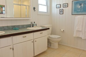 A bathroom with a white sink, toilet, and vanity with cabinets. There is a window above the toilet and a towel rack on the wall. - South Beach: A Perfect Beachfront Getaway - Pool, beachfront, ocean views, (Hope Town Bahamas)