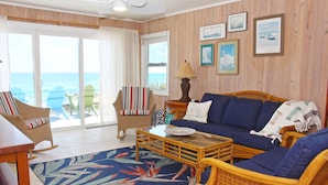 A living room with a view of the ocean, a wicker sofa, a striped armchair, and a coffee table. - South Beach: A Perfect Beachfront Getaway - Pool, beachfront, ocean views, (Hope Town Bahamas)