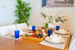 A dining table set with plates, blue glasses, a wooden board with food, and a vase with flowers.