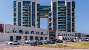 Un bâtiment moderne doté d’une arche centrale, de nombreux balcons et d’un espace de stationnement où sont garées plusieurs voitures.