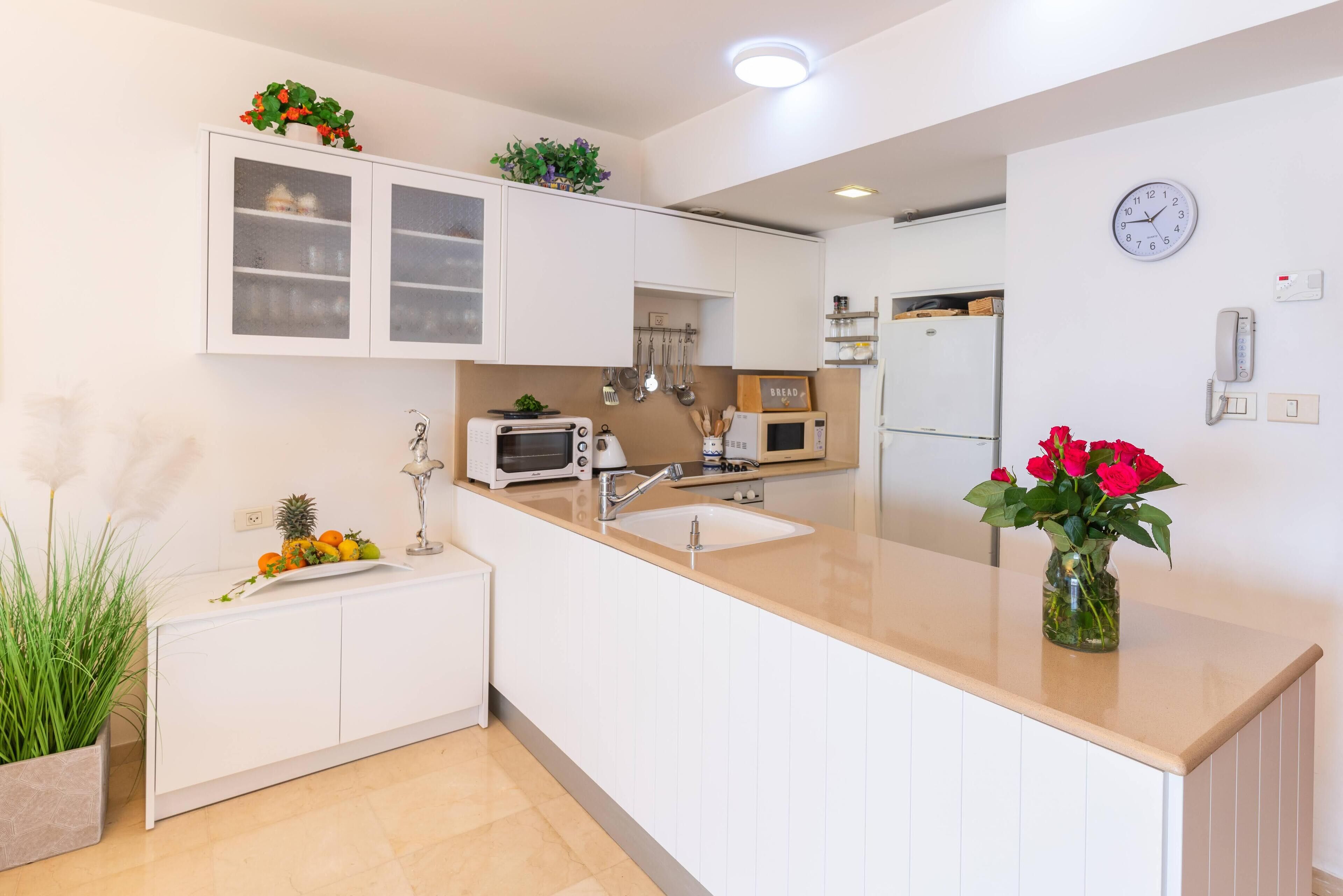 Une cuisine moderne avec des meubles blancs, un évier, un four à micro-ondes et une horloge au mur.