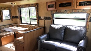 A compact RV interior with a kitchenette, a dining area, and a seating area with a black leather couch.