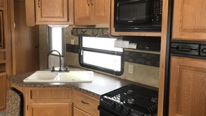 A compact kitchen with wooden cabinets, a built-in microwave, a stove, and a window.
