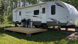 A recreational vehicle (RV) parked in a wooded area with a small wooden platform in front.