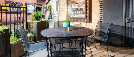 An outdoor seating area with a round table and metal chairs, surrounded by brick walls and potted plants.