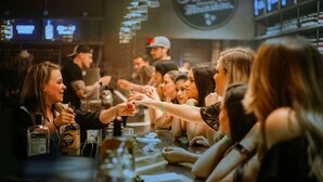 A bar setting with people engaged in conversation, bottles of whiskey, and a menu on the counter. - *Studio Loft*Walk to Broadway*Printers Alley Lofts (Nashville)