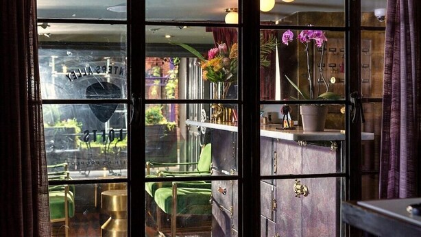 A room with a large window, a green chair, a small table, and a cabinet with brass handles. - *Studio Loft*Walk to Broadway*Printers Alley Lofts (Nashville)