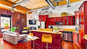 A modern kitchen with red cabinets, a wooden ceiling, and a bar area with stools. - *Studio Loft*Walk to Broadway*Printers Alley Lofts (Nashville)