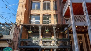 A multi-story building with a brick facade, a ground-floor entrance with a green door, and a balcony with hanging plants. - *Studio Loft*Walk to Broadway*Printers Alley Lofts (Nashville)