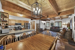 Un intérieur rustique avec une table à manger en bois, une cuisine dotée de plans de travail en granit et un salon chaleureux avec une cheminée.