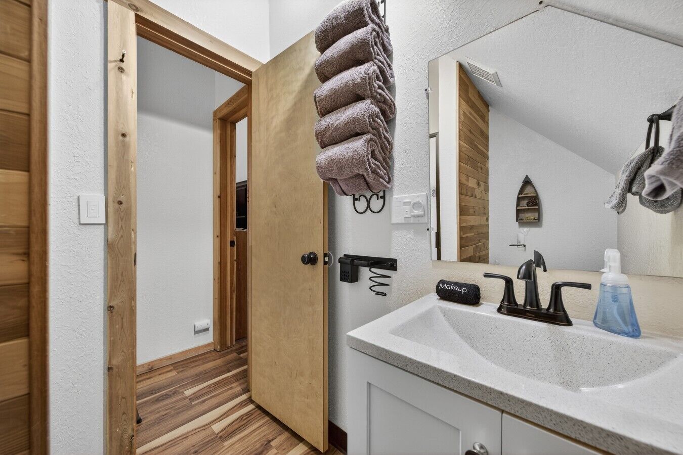Een badkamer met een houten deur, een wastafel met spiegel en handdoeken aan de muur.