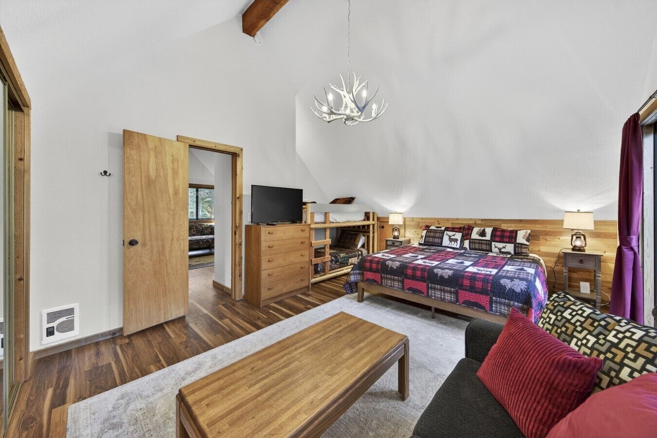 A cozy bedroom with a bed, a TV, a wooden dresser, a desk, and a chandelier.