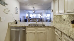 A kitchen with a dishwasher, granite countertop, and white cabinets.