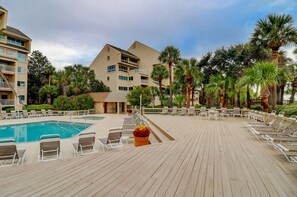 A pool area with lounge chairs and a pool, surrounded by palm trees and a building with multiple balconies.