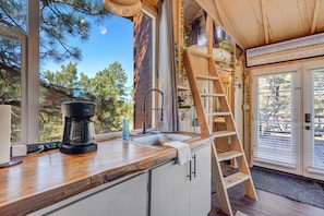 Une cuisine avec un plan de travail en bois, une machine à café, un évier et une échelle.