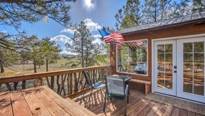 Une terrasse en bois avec une table et des chaises, une porte vitrée donnant sur un beau paysage et un drapeau américain.