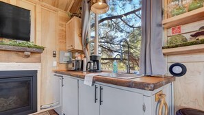 Une cuisine chaleureuse avec des meubles en bois, une cuisinière encastrée et une fenêtre donnant sur les arbres.