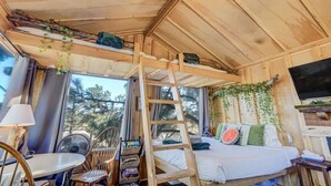 Une cabane chaleureuse avec un lit superposé, une échelle, une table avec des chaises et un téléviseur.