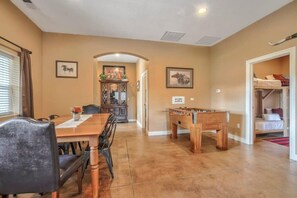 Uma sala de jantar com mesa e cadeiras de madeira, mesa de futebol e um corredor que leva a um quarto.