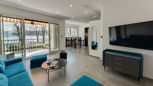 A modern living room with a large TV, blue sofas, a glass coffee table, and a view of a balcony with a railing. - Swan Lake - Design apartment facing Lake Annecy (Annecy)