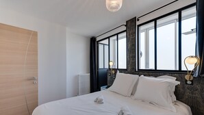 A modern hotel room with a large bed, two bedside lamps, a window with a view, and a radiator. - Swan Lake - Design apartment facing Lake Annecy (Annecy)