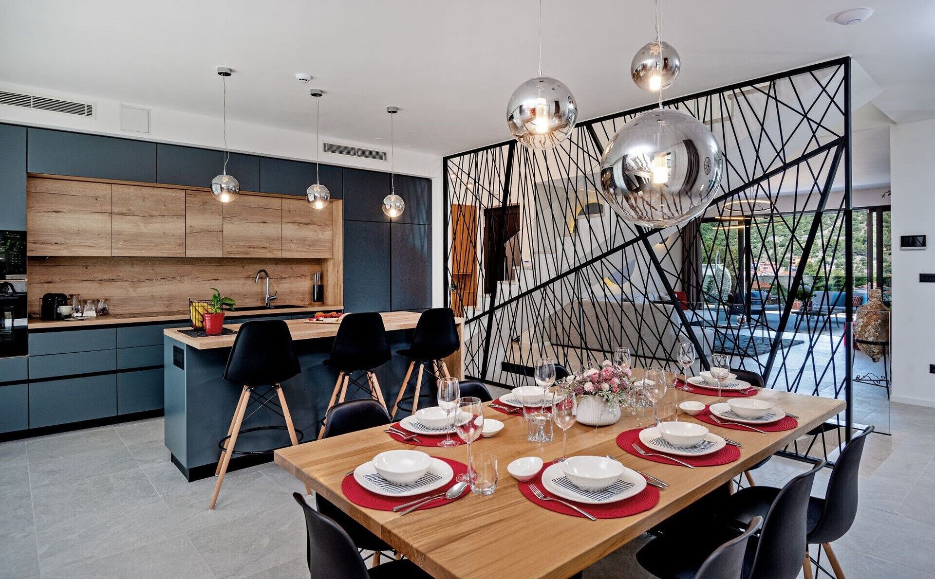 A modern kitchen with wooden cabinets, a dining area with a wooden table set for six, and a decorative black partition.