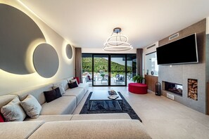 A modern living room with a sofa, coffee table, TV, fireplace, and a view of a hillside.