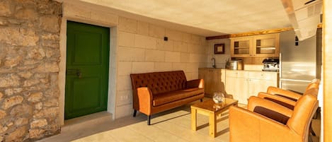 A cozy living room with a sofa and chairs, a coffee table, and a kitchen area with cabinets and appliances.